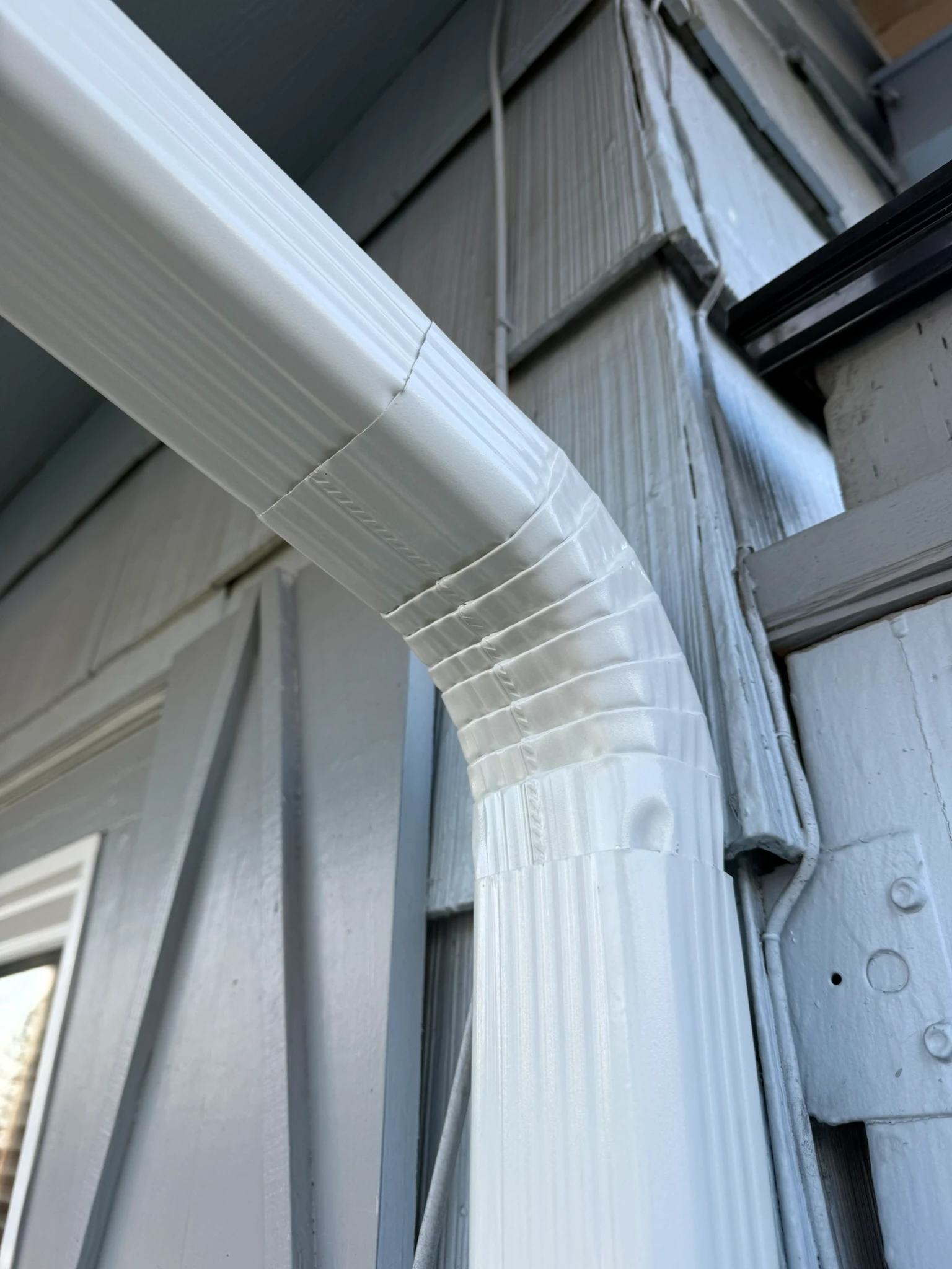Downspout elbow secured to siding with color-matched straps